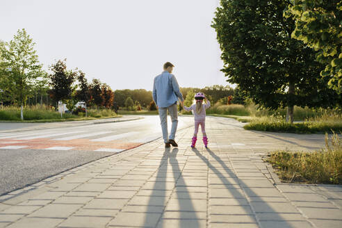 Mann hält die Hand seiner Tochter beim Rollschuhlaufen auf dem Gehweg - NSTF00041