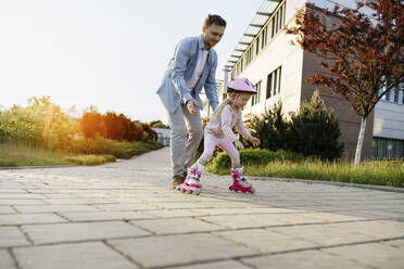 Vater hilft seiner Tochter beim Rollschuhlaufen auf dem Gehweg - NSTF00042