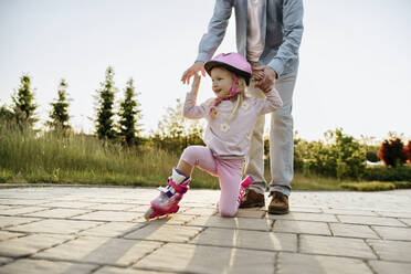 Father helping daughter wearing roller skates on footpath - NSTF00043