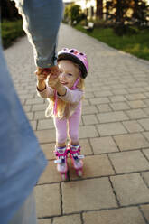 Hand of man assisting daughter doing roller skate on footpath - NSTF00051