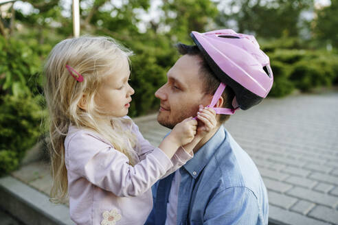 Daughter fastening sports helmet on father at park - NSTF00058