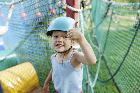 Nettes Mädchen trägt Helm und zeigt Daumen hoch Geste am Seil Park - NSTF00060
