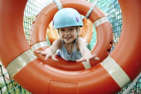 Lächelndes Mädchen mit Helm und Hindernisparcours im Seilpark - NSTF00063