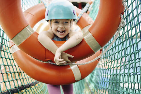 Happy cute girl hanging on circle equipment at rope park - NSTF00064