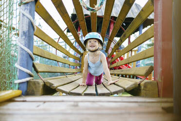 Smiling girl crawling inside wooden tunnel at rope park - NSTF00067