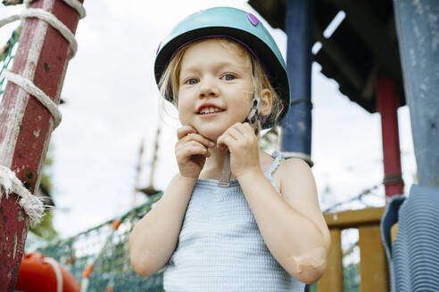 Smiling girl fastening sports helmet at rope park - NSTF00068