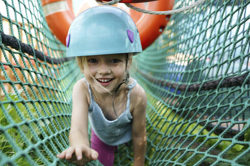 Lächelndes Mädchen krabbelt auf dem Netz im Abenteuerpark - NSTF00070