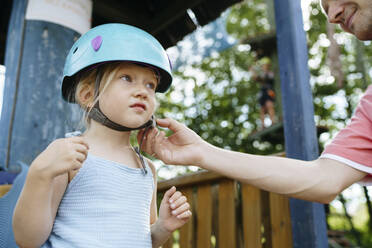 Father fastening helmet of daughter at rope park - NSTF00071