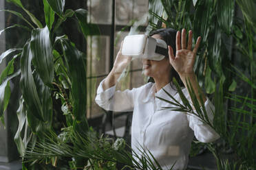 Businesswoman gesturing with virtual reality simulator in office - YTF02028