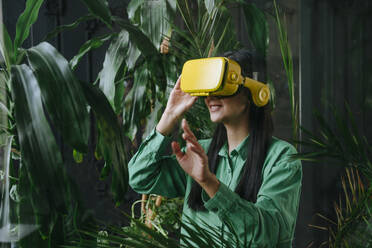 Businesswoman wearing yellow virtual reality simulator near plants - YTF02031