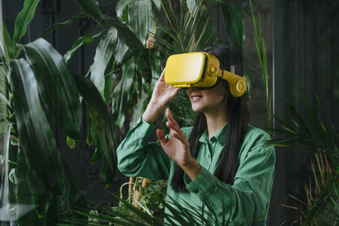 Geschäftsfrau trägt gelben Virtual-Reality-Simulator in der Nähe von Pflanzen - YTF02031