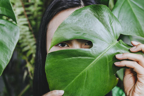 Frau versteckt Gesicht mit Monstera-Blatt - YTF02038