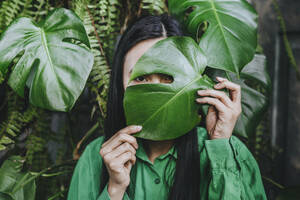 Junge Frau versteckt Gesicht mit Monstera-Blatt - YTF02039