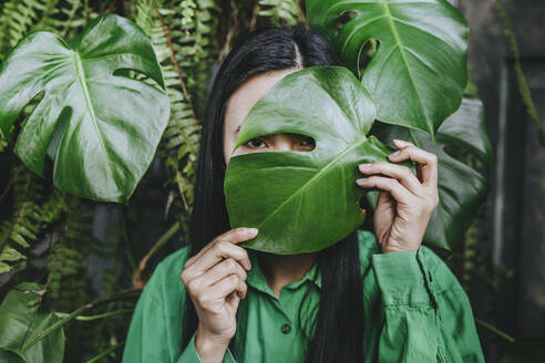 Young woman hiding face with monstera leaf - YTF02039