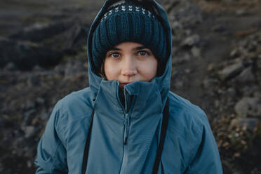 Woman in a blue jacket and beanie gazes at the camera with a subtle smile in an Icelandic setting. - ADSF53338