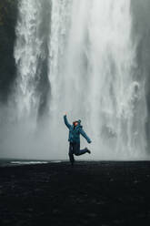 A female traveler expresses joy with a mid-air jump before the powerful backdrop of an Icelandic waterfall, capturing the thrill of exploration. - ADSF53342