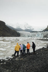 Rückenansicht einer Gruppe von Touristen, darunter Männer und Frauen, die vor der atemberaubenden Eislandschaft einer Gletscherlagune in Island stehen. - ADSF53347