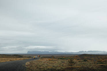 A group of unrecognizable explorers, including a man and a woman, trekking on a secluded path in the dramatic and wide landscapes of Iceland, under a vast cloudy sky. - ADSF53348