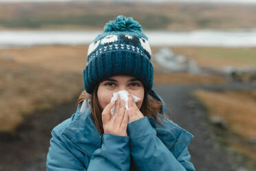 Woman in a cold Iceland setting, blowing her nose with a tissue. - ADSF53350