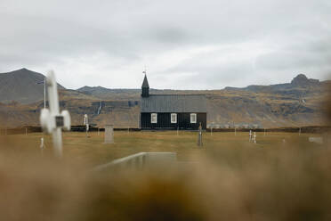 A quaint black church stands alone amidst the dramatic terrain of Iceland, likely the Búðakirkja in Búðir, with majestic mountains in the background. - ADSF53352