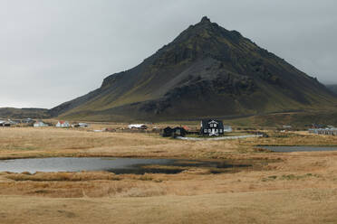 An idyllic Icelandic village nestles at the base of a towering, rugged mountain, highlighting the serene landscape of Iceland. - ADSF53353