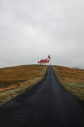 A lone road leading to a picturesque church on a hill in Iceland, under an overcast sky. - ADSF53355