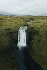 A captivating and isolated waterfall cascades down into a serene pool amidst the verdant hills of Iceland, showcasing the country's stunning natural beauty. - ADSF53357