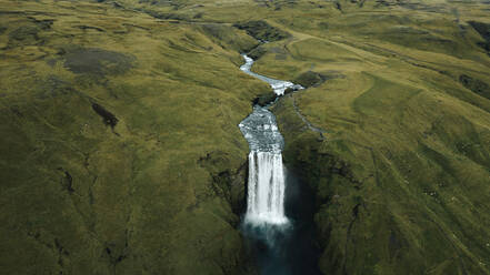 From above captivating and isolated waterfall cascades down into a serene pool amidst the verdant hills of Iceland, showcasing the country's stunning natural beauty. - ADSF53358