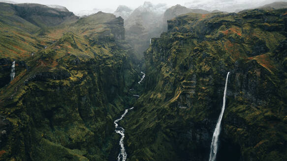 From above majestic aerial view of a cascading waterfall in Iceland's rugged landscape enveloped in mist. - ADSF53363