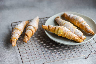 Freshly baked homemade pastry cones filled with sweet jam, dusted with powdered sugar, served on a ceramic plate with a cooling rack on a grey countertop - ADSF53393