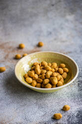 Bowl of salty coated peanuts on a textured surface with some scattered around the bowl - ADSF53399