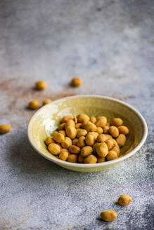 Bowl of salty coated peanuts on a textured surface with some scattered around the bowl - ADSF53399