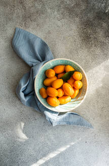 From above of fresh kumquats in a decorative bowl with a blue napkin on a textured concrete background - ADSF53418