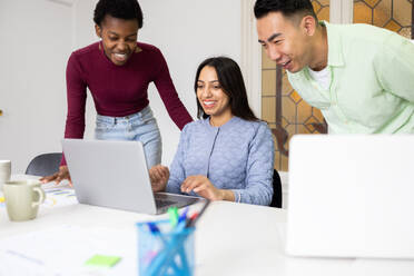 Three colleagues working together with a laptop in a bright office setting, sharing ideas and collaborating on a project. - ADSF53603