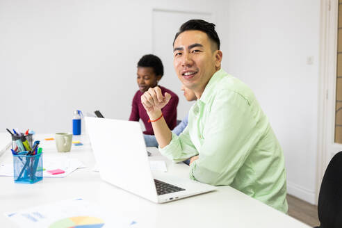A smiling Asian man in a casual green shirt participates in an office meeting with colleagues, creating a vibrant and collaborative work atmosphere. - ADSF53605