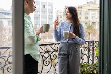 Two people enjoying a relaxed coffee break together on a balcony overlooking an urban background. - ADSF53625