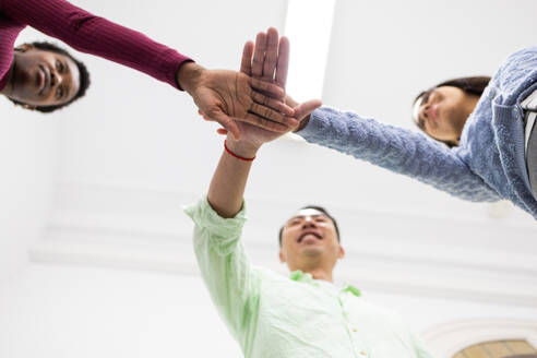 Diverse group of people stack hands together, signaling teamwork, unity, and collaboration in a light-filled room. - ADSF53629