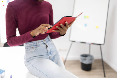 Professional in a burgundy sweater uses a tablet in a modern office. - ADSF53642