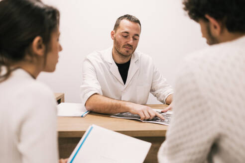 A medical professional examines an X-ray film while discussing the findings with a focused patients during a consultation in a clinic office. - ADSF53662