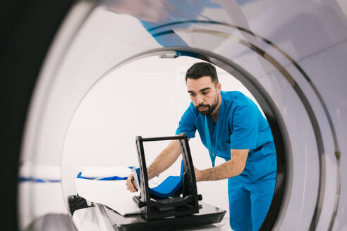 A focused medical technician is calibrating an MRI scanner in a modern healthcare facility to prepare for patient diagnostics. - ADSF53674