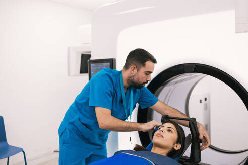 Male technician assisting a female patient before a computed tomography scan in a modern clinical setting. - ADSF53675