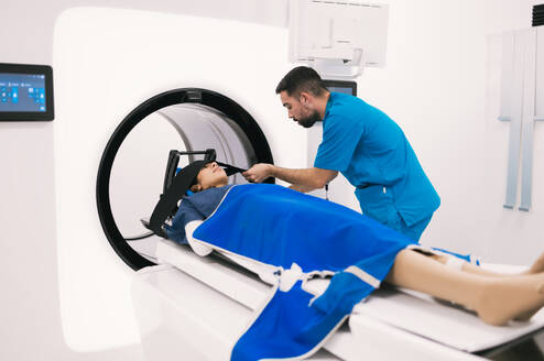 Male technician assisting a female patient before a computed tomography scan in a modern clinical setting. - ADSF53679