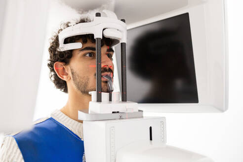 Ein junger männlicher Patient erhält eine Panorama-Röntgenaufnahme mit modernen medizinischen Geräten. - ADSF53681