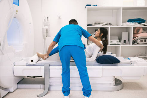 A healthcare professional is seen assisting a patient onto an MRI scanner in a bright clinical setting. - ADSF53682