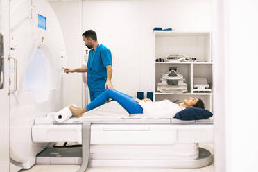 A healthcare worker is preparing an MRI scan for a female patient lying on the machine table. - ADSF53684