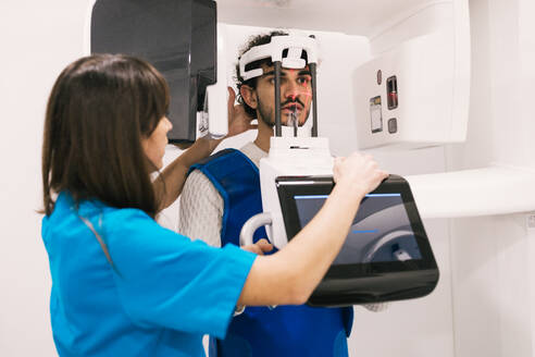 Dental professional assists a male patient with a 3D x-ray scan in a clinic. - ADSF53687