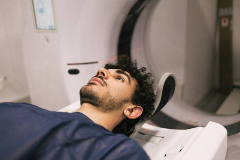 A young adult male is pictured lying down, preparing for an MRI scan in a modern medical imaging room. - ADSF53688