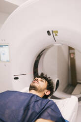 A young male patient lies in a CT scanner during a medical imaging procedure, with focus on advanced healthcare technology. - ADSF53689