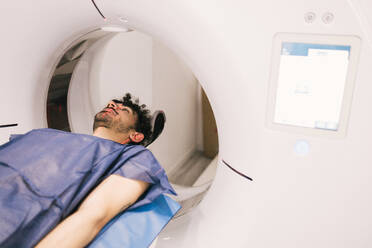A male patient lies still in a CT scanner during a diagnostic radiological procedure at a healthcare center. - ADSF53690