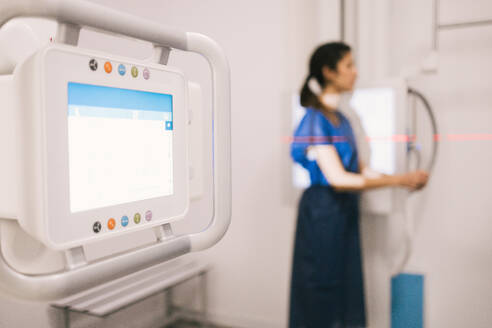 A healthcare worker stands next to modern x-ray machinery in a medical facility, preparing for a diagnostic procedure. - ADSF53692